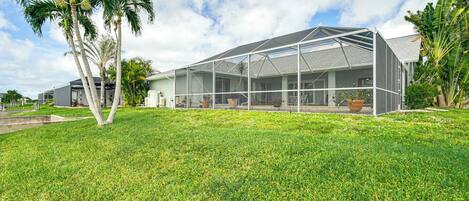 A modern house with a large covered patio area, surrounded by well-maintained grass and palm trees.