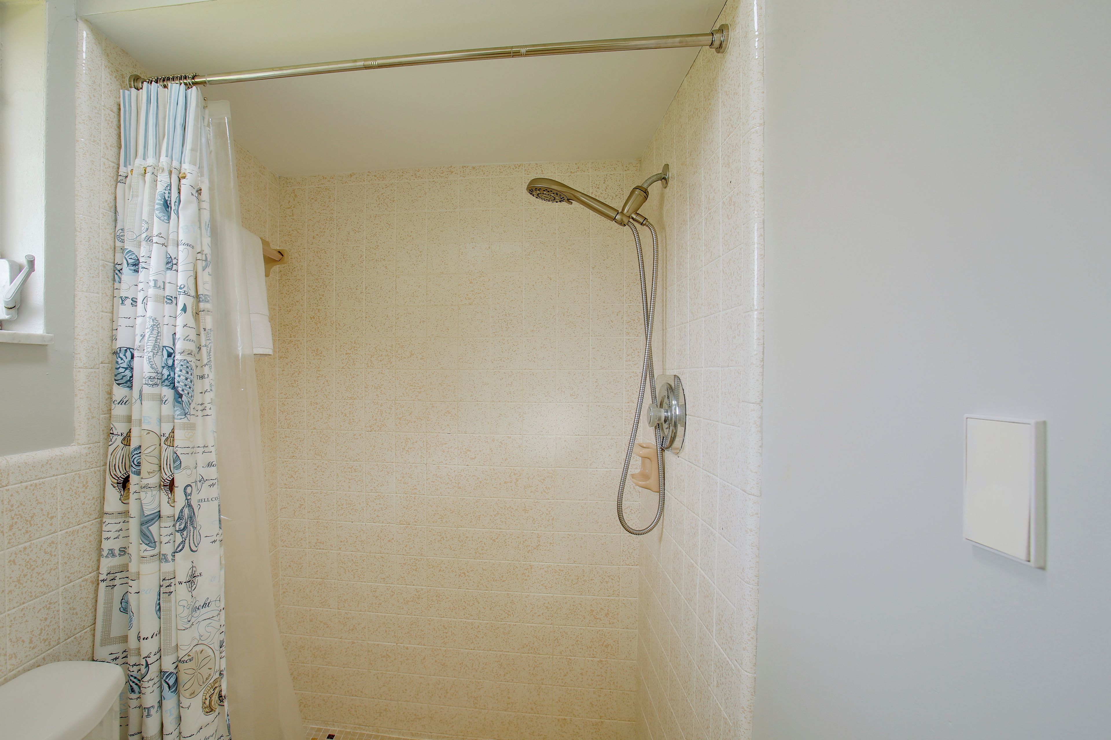 A shower with a handheld showerhead and a curtain.