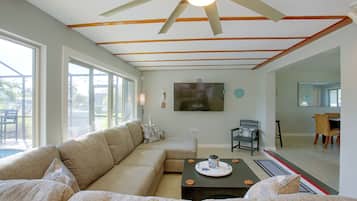 Ein geräumiges Wohnzimmer mit einer großen Eckcouch, einem flachbildfernseher an der Wand und einem Deckenventilator.