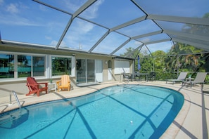 A swimming pool with a glass enclosure, surrounded by lounge chairs and a patio area.