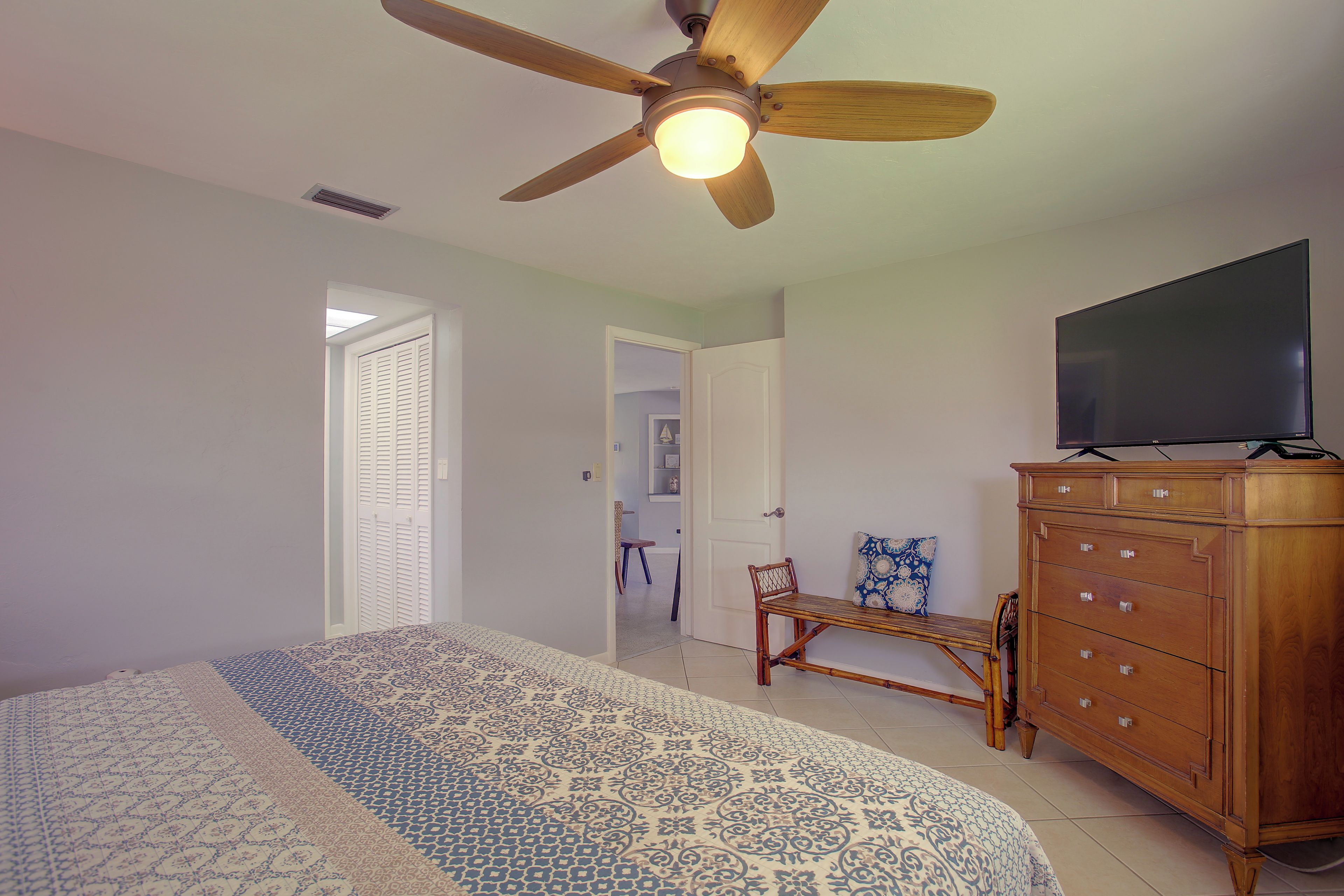 A bedroom with a bed, a wooden dresser, a television, and a ceiling fan.
