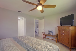A bedroom with a bed, a wooden dresser, a television, and a ceiling fan.