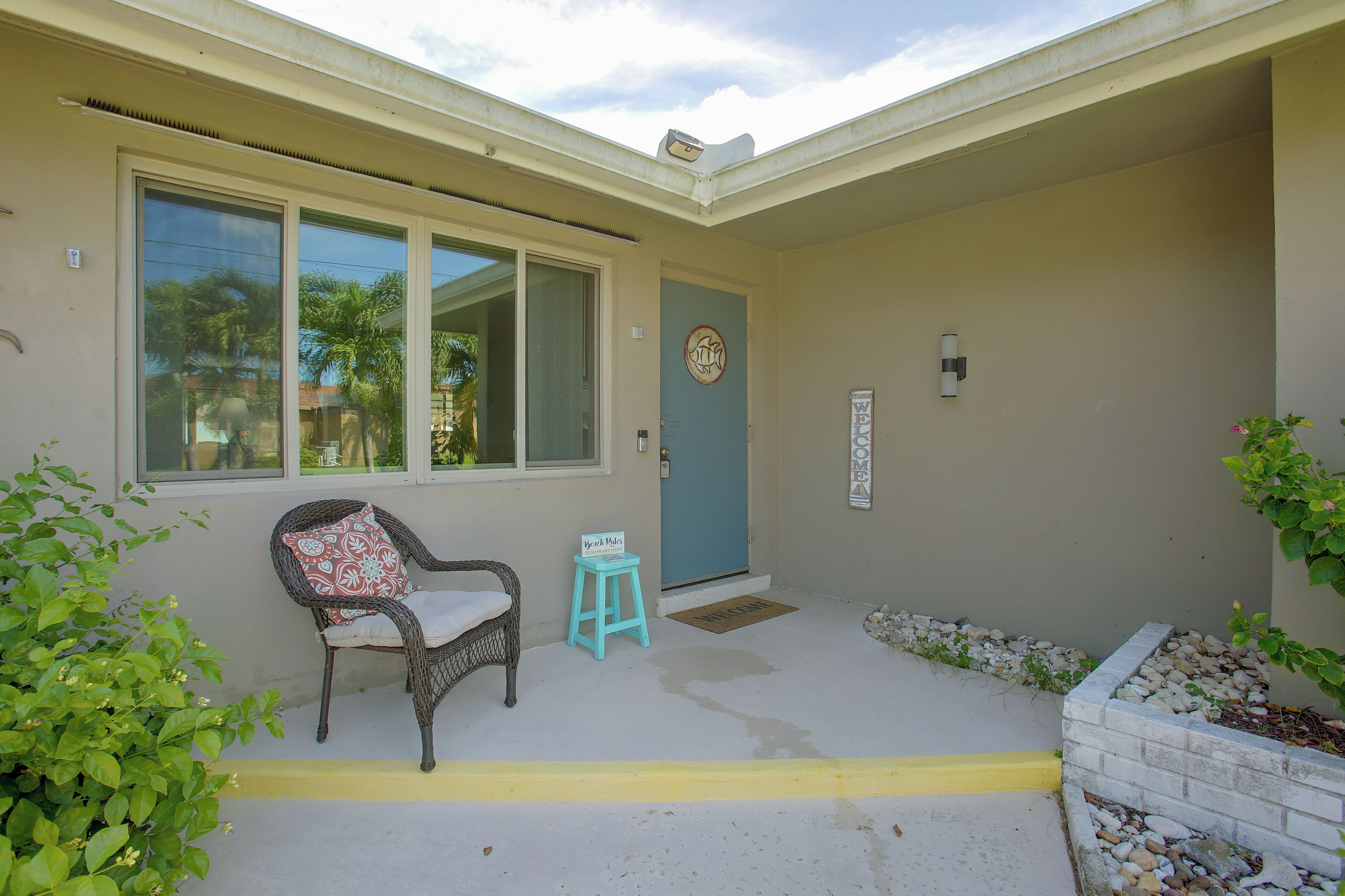 A house with a porch, a chair, a small table, a welcome mat, and a sign.