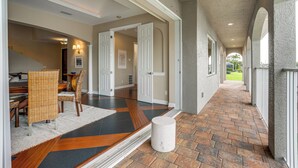 A hallway with a patterned floor, a dining area with wicker chairs, and a door leading to another room.