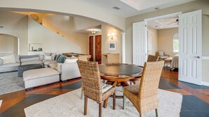 A spacious living room with a large round table, comfortable seating, and a staircase leading to an upper level.