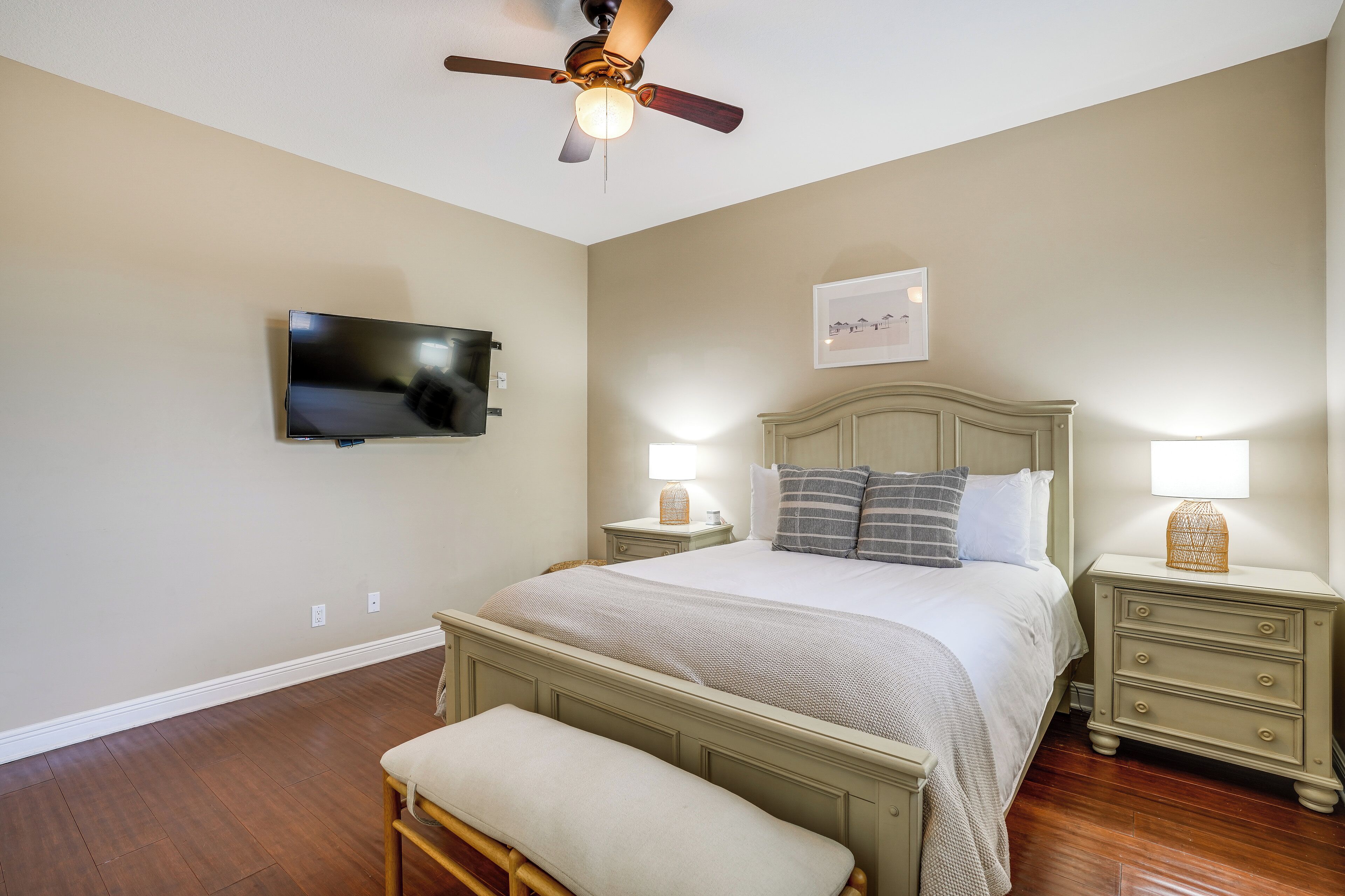 A bedroom with a bed, bedside tables, a TV, a ceiling fan, and a bench.