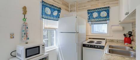 Cocina compacta con electrodomésticos blancos, encimera de granito y adornos de ventana azules con estampado.