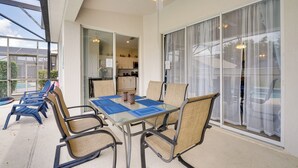 A sunlit patio with a glass table, chairs, and a ceiling fan.