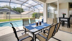 A covered patio with a pool, dining table, chairs, and a kitchen area.