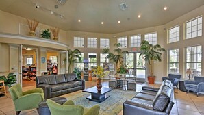 A spacious lobby with a leather sofa, green armchairs, a coffee table, and a large window overlooking the outdoors.