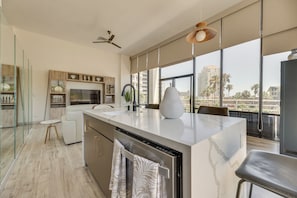 A modern kitchen with a large island, a dining area with a high ceiling fan, and a view of palm trees through large windows. - South Padre Island Gem: Community Pool & Hot Tub! (South Padre Island)