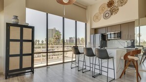 A modern kitchen with a large window, a microwave, and a refrigerator. There are three bar stools and a cabinet with decorative items. - South Padre Island Gem: Community Pool & Hot Tub! (South Padre Island)