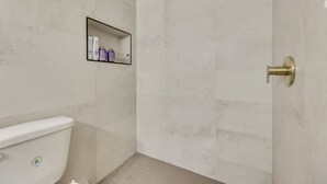 A bathroom with a toilet, a shower area, and a shelf with toiletries. - South Padre Island Gem: Community Pool & Hot Tub! (South Padre Island)
