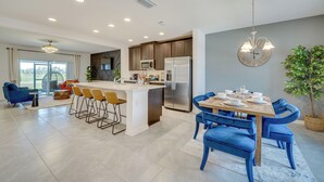 A modern kitchen with a central island, a dining area with blue chairs, and a large window. - Davenport Home ~ 15 Mi to Disney World! (Davenport)