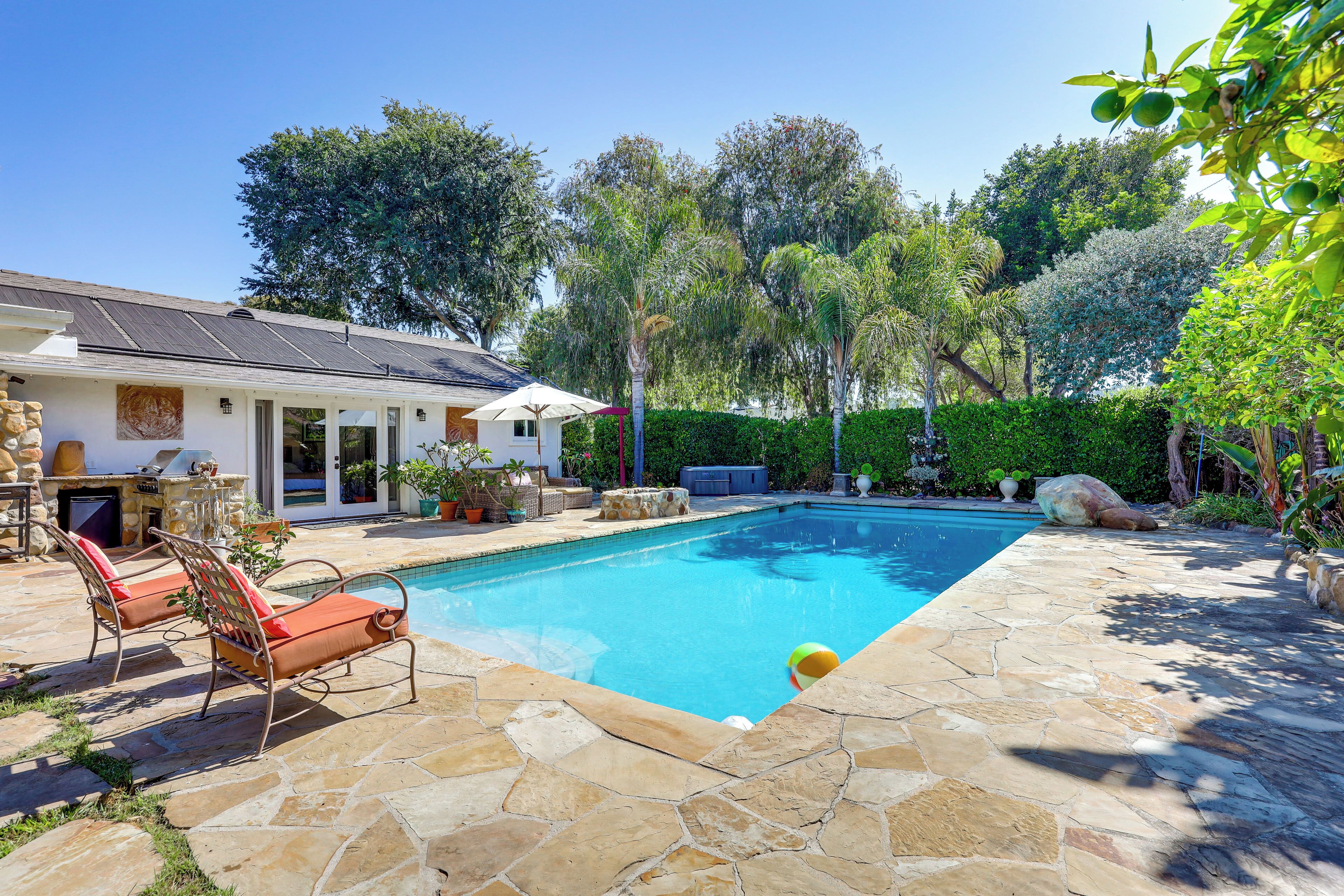 A swimming pool with stone tiles, lounge chairs, and a covered patio area.