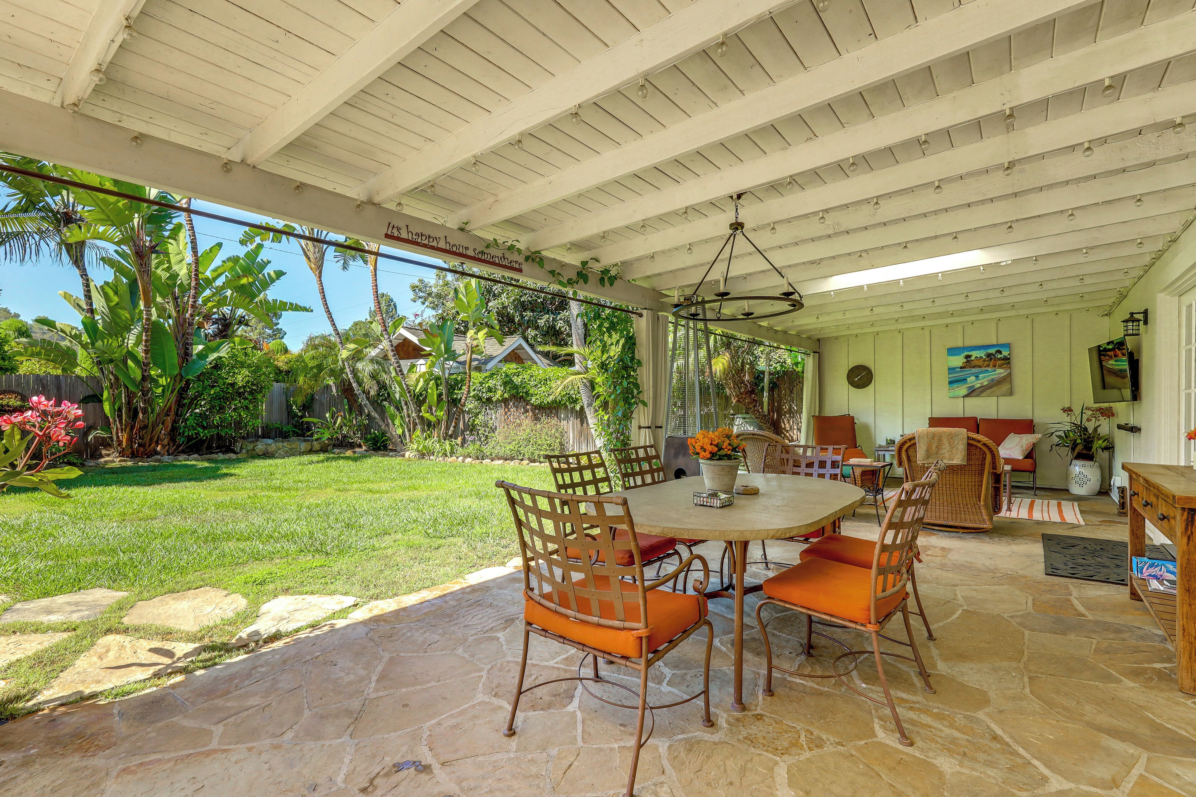 A covered patio area with a stone floor, outdoor furniture, and a view of a lush garden.