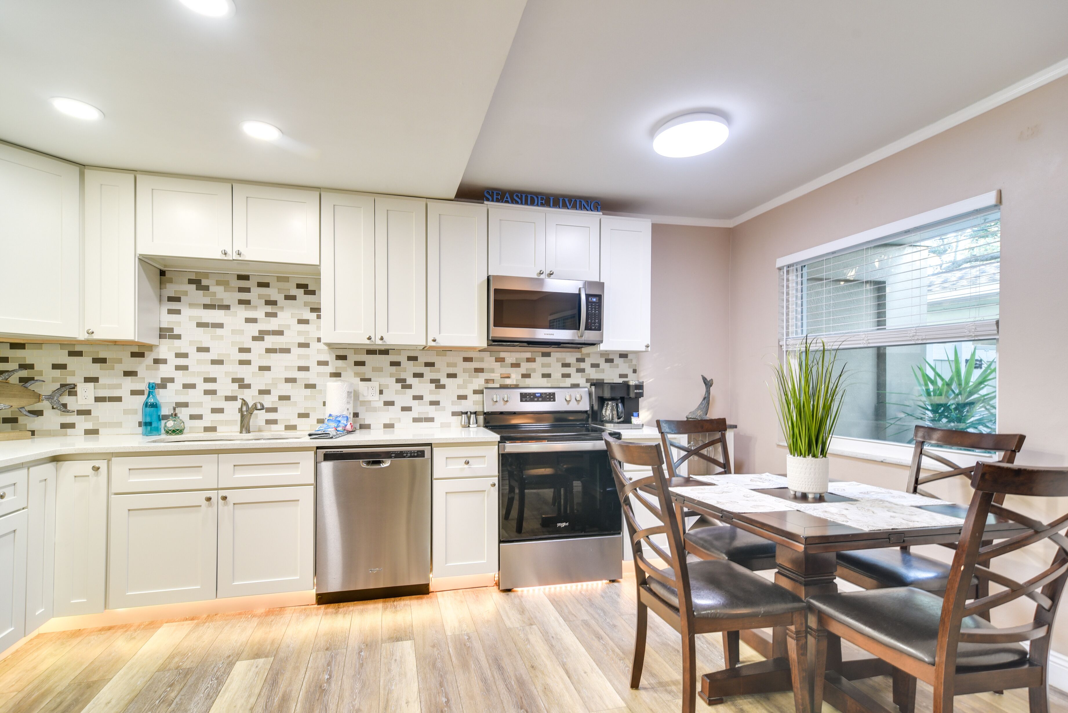 A modern kitchen with white cabinets, a stainless steel dishwasher, an oven, and a microwave.