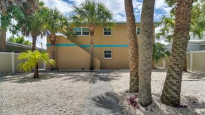 A pathway leading to a building with a beige facade and blue trim. - Indian Rocks Beach Escape: Beach Gear, Near Ocean! (Indian Rocks Beach)