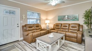 A living room with two brown leather sofas, a white coffee table, a ceiling fan, a window with blinds, a lamp, and wall art. - Indian Rocks Beach Escape: Beach Gear, Near Ocean! (Indian Rocks Beach)