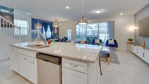 A modern kitchen with granite countertops, a dishwasher, and a dining area with a blue sofa and a TV. - Pool, Games & Disney Magic! Epic Family Oasis (Davenport)