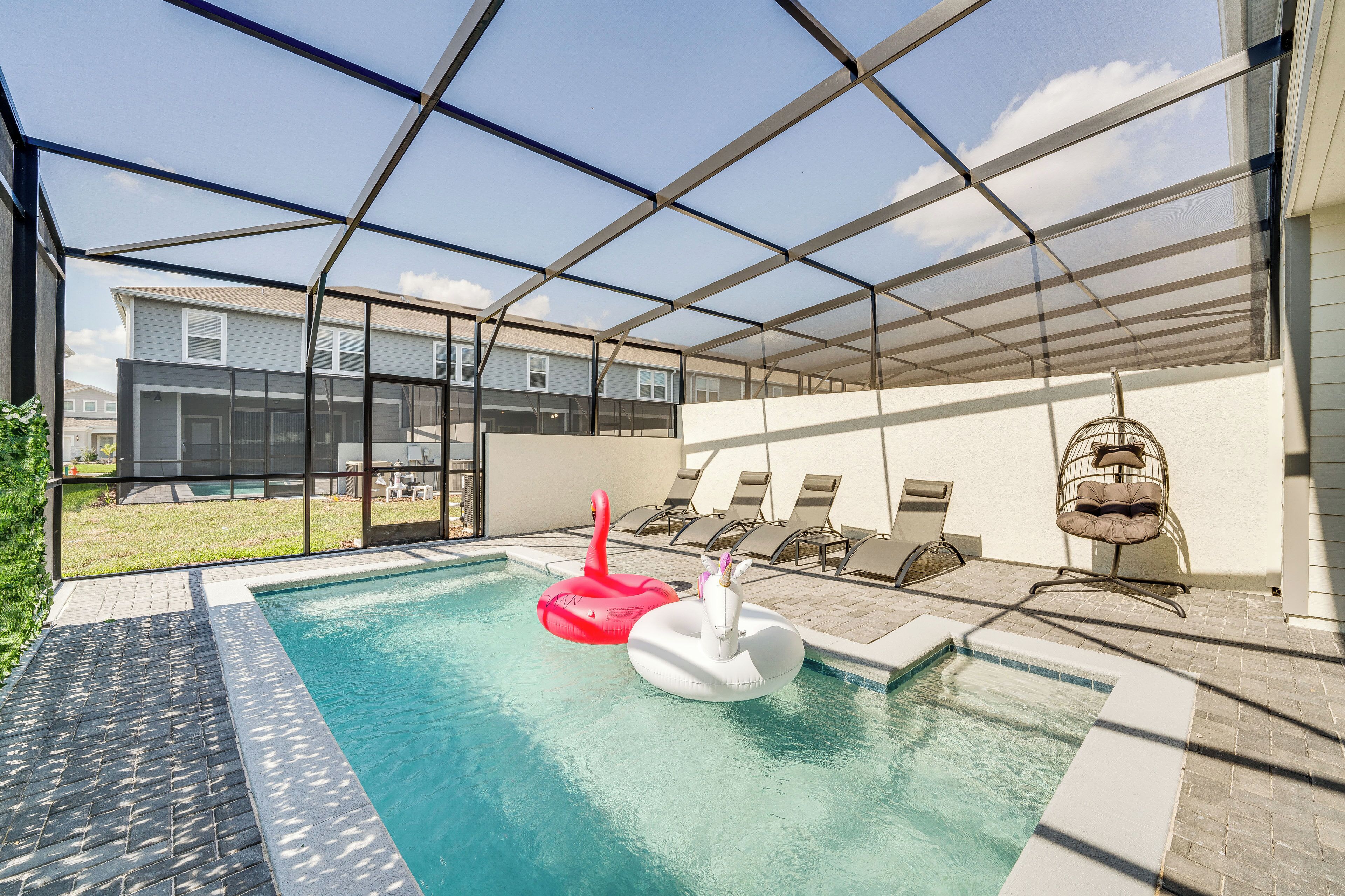 Une piscine intérieure avec deux jeux gonflables, un patio couvert avec des chaises longues, et une vue sur des immeubles résidentiels en arrière-plan.