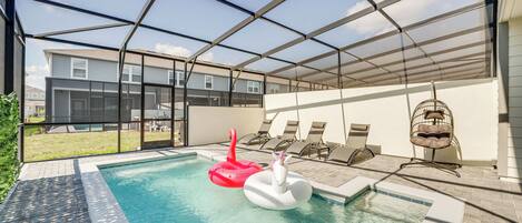 Une piscine intérieure avec deux jeux gonflables, un patio couvert avec des chaises longues, et une vue sur des immeubles résidentiels en arrière-plan.