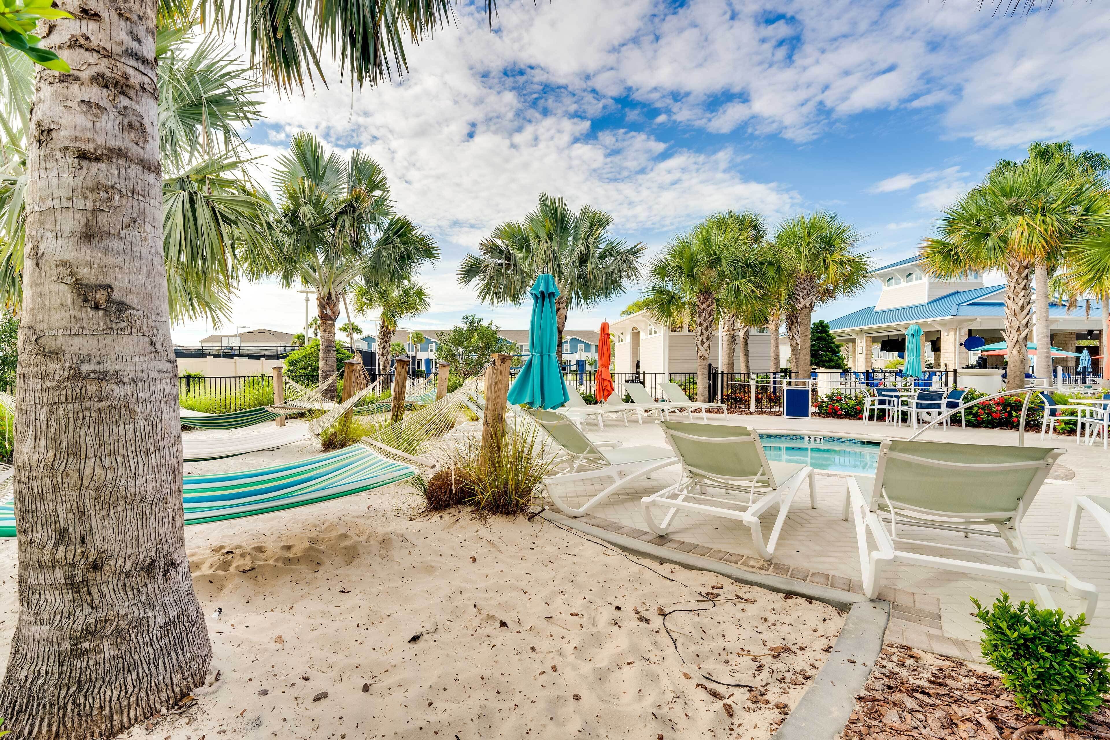 A pool area with lounge chairs, a hammock, and palm trees.