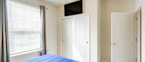 A bedroom with a bed, a window with curtains, a white door, and a mounted television.