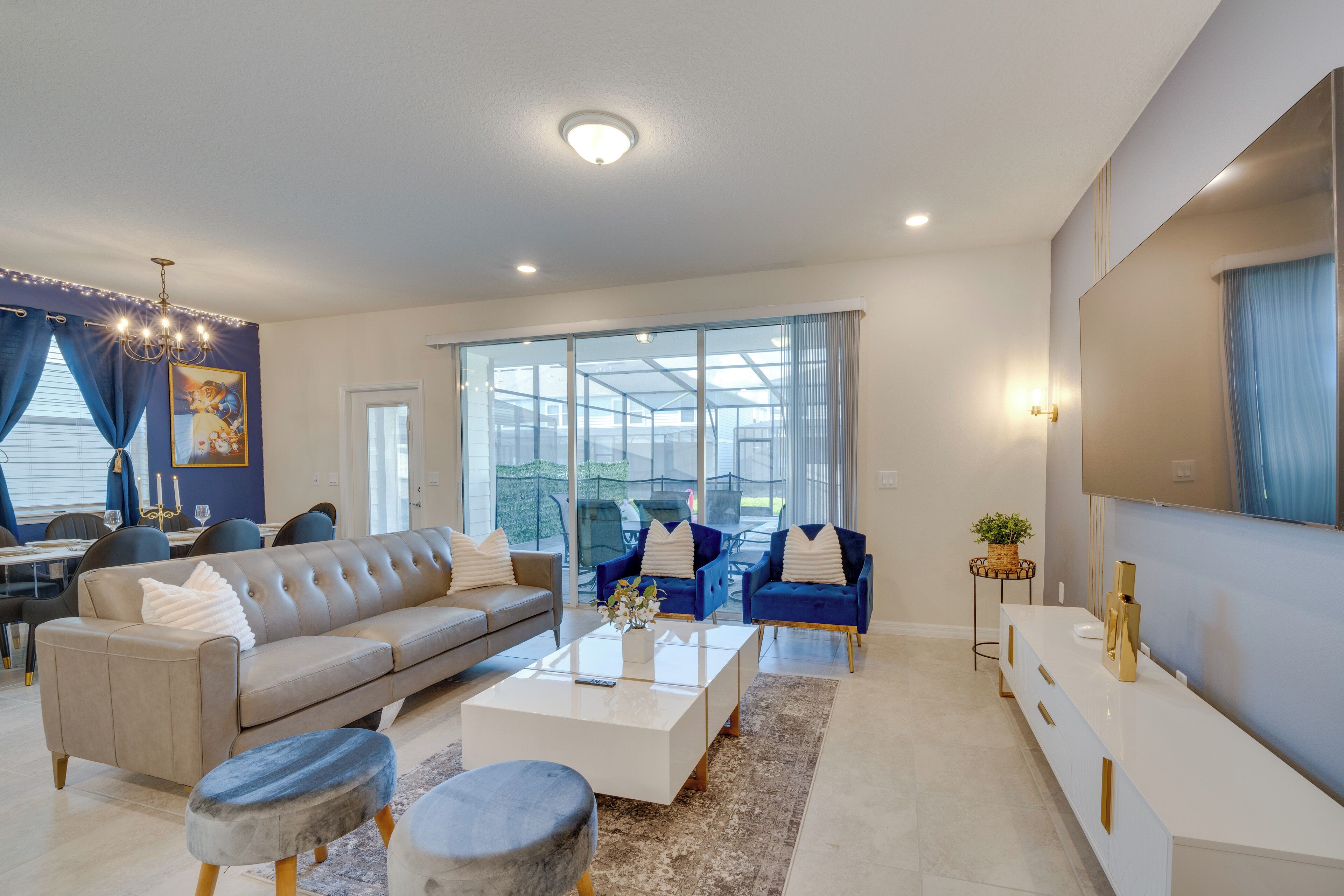 A modern living room with a sofa, coffee table, and chairs, large windows, and a dining area.