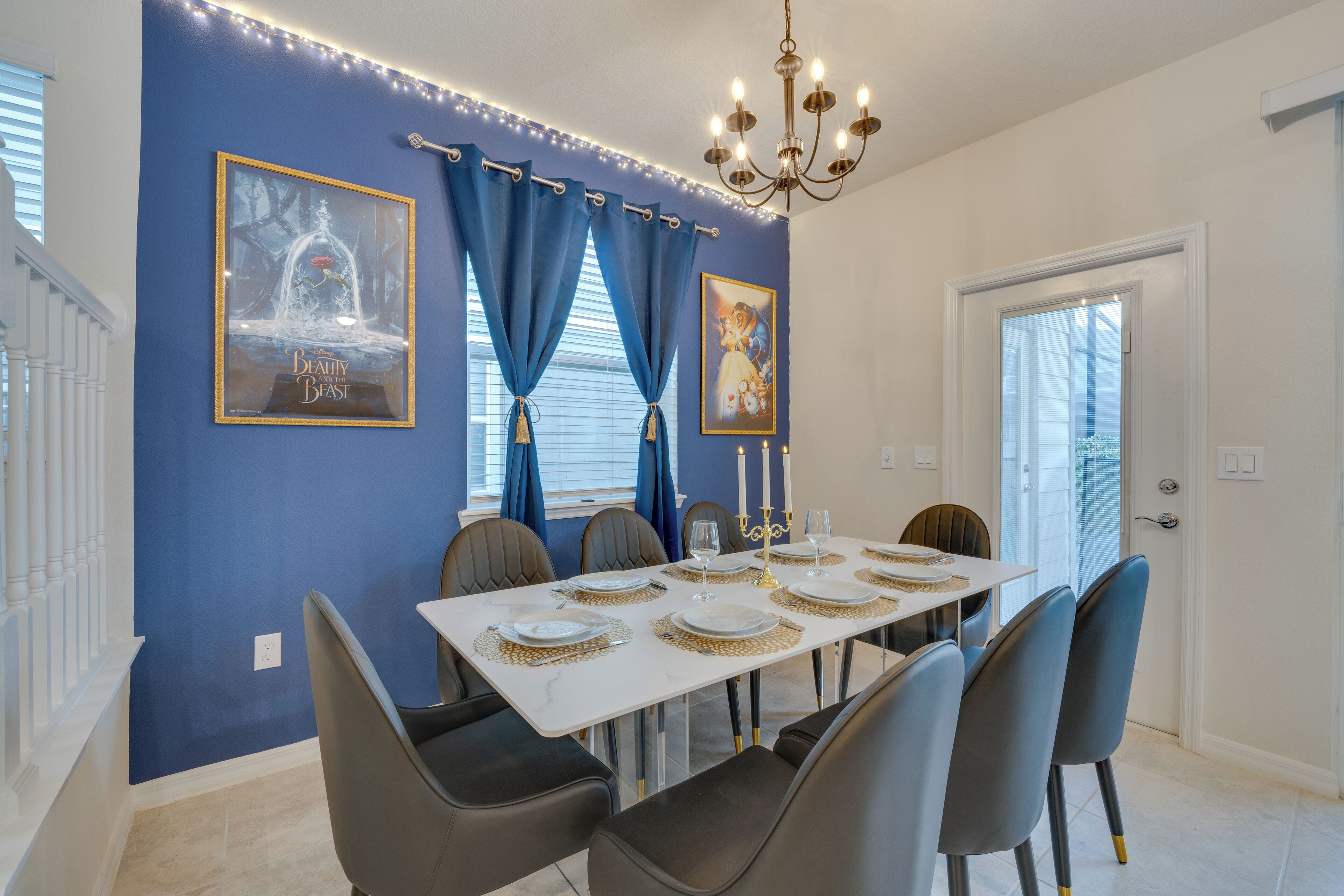A dining area with a white table set for six, blue curtains, and two framed pictures on the wall.