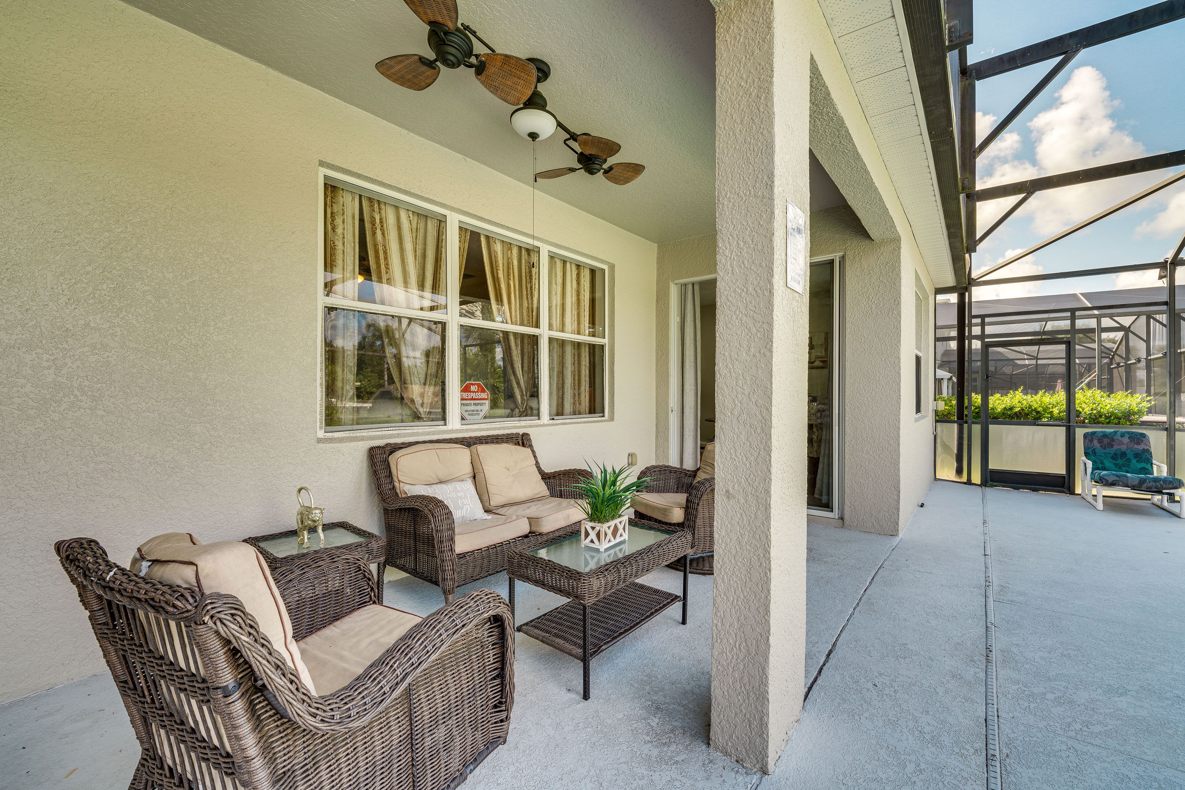 A covered patio area with wicker furniture, a glass table, and a ceiling fan.