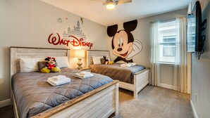 A hotel room with two beds, a ceiling fan, Mickey Mouse wall decal, and a TV on the wall. - Spacious Kissimmee Escape, Close to Disney World! (Kissimmee)
