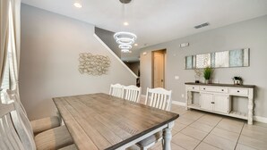 A dining area with a wooden table and white chairs, a white console table with a plant, and a wall-mounted abstract art piece. - Spacious Kissimmee Escape, Close to Disney World! (Kissimmee)