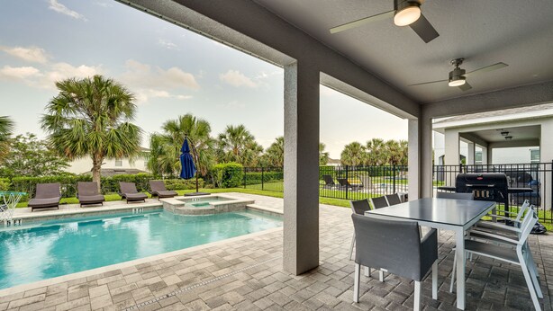 A pool area with a table and chairs, surrounded by lounge chairs and palm trees. - Spacious Kissimmee Escape, Close to Disney World! (Kissimmee)