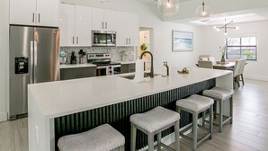 A modern kitchen with a central island, bar stools, stainless steel appliances, and pendant lighting. - Private Pool & Grill: Cape Coral Vacation Rental! (Cape Coral)