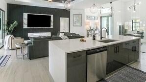 A modern kitchen with a central island, built-in dishwasher, and a dining area with a sofa and coffee table. - Private Pool & Grill: Cape Coral Vacation Rental! (Cape Coral)