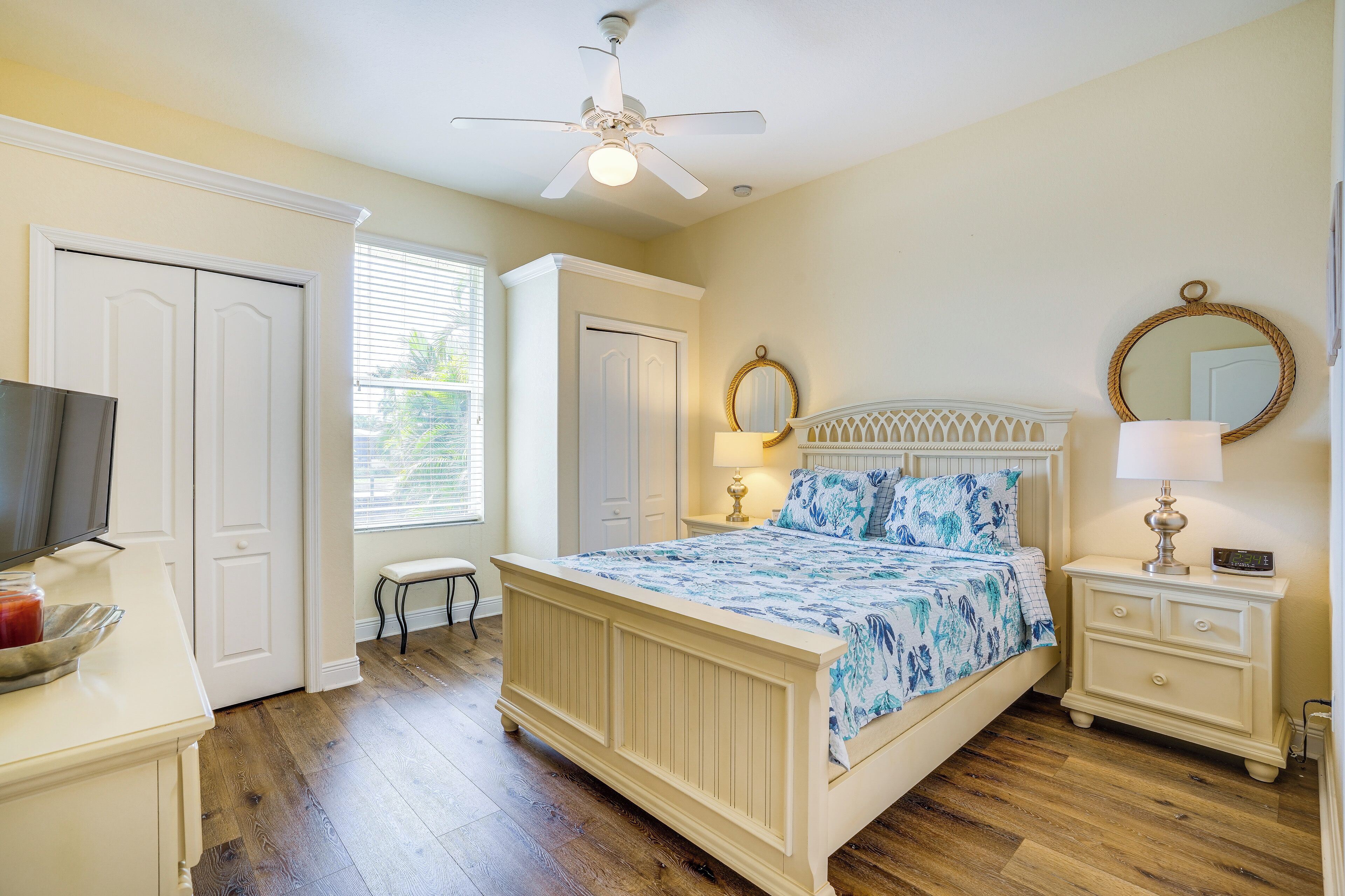 A bedroom with a bed, nightstands, a ceiling fan, a TV, and a window with blinds.