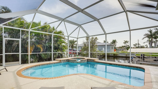 An indoor swimming pool with a glass ceiling, surrounded by palm trees and a view of a house.