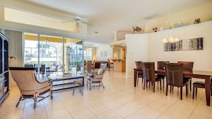A spacious dining area with a large table and multiple chairs, a ceiling fan, and a view through large glass doors to the outdoors.