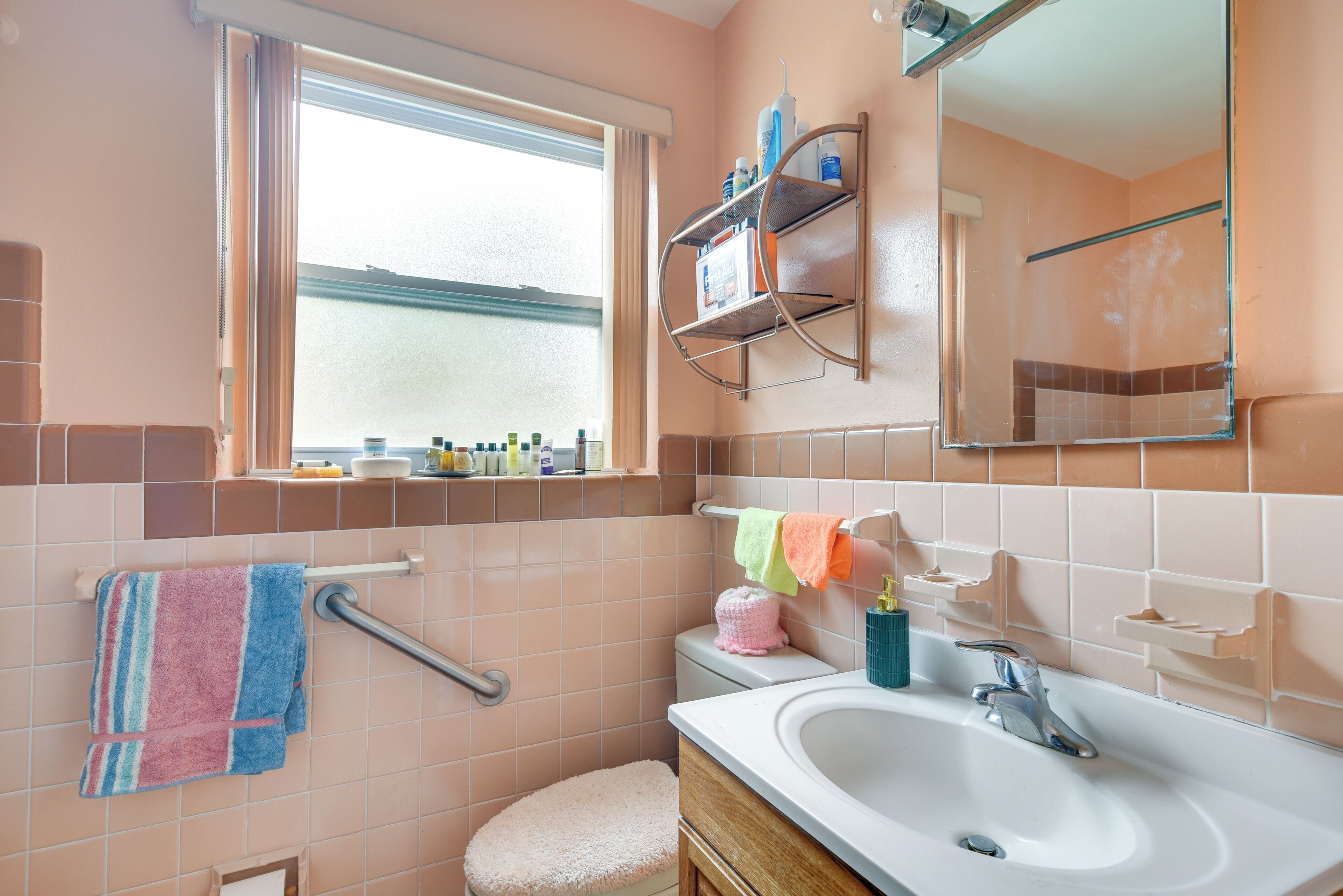 Une salle de bain avec une fenêtre, un lavabo, un miroir et un porte-serviettes.
