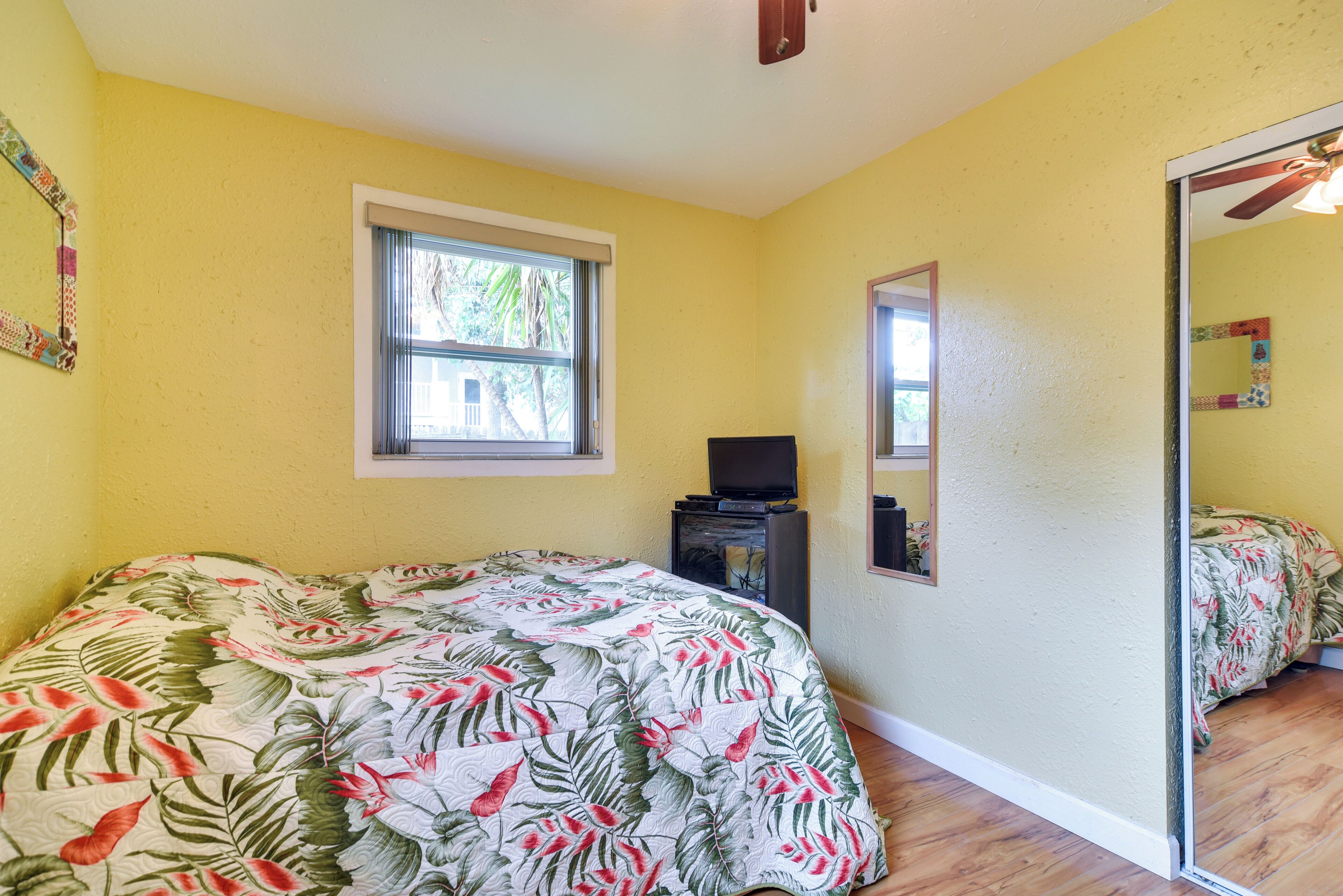 A bedroom with a bed, a window, a mirror, and a television.