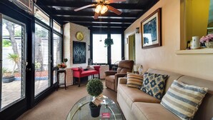 Un salon chaleureux avec un ventilateur de plafond, une table basse en verre, un canapé beige et un fauteuil rouge.