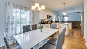 A modern kitchen with white cabinets, a central island, and a dining area with a white table and grey upholstered chairs. - Disney-area Home w/ Private Pool in Davenport! (Davenport)