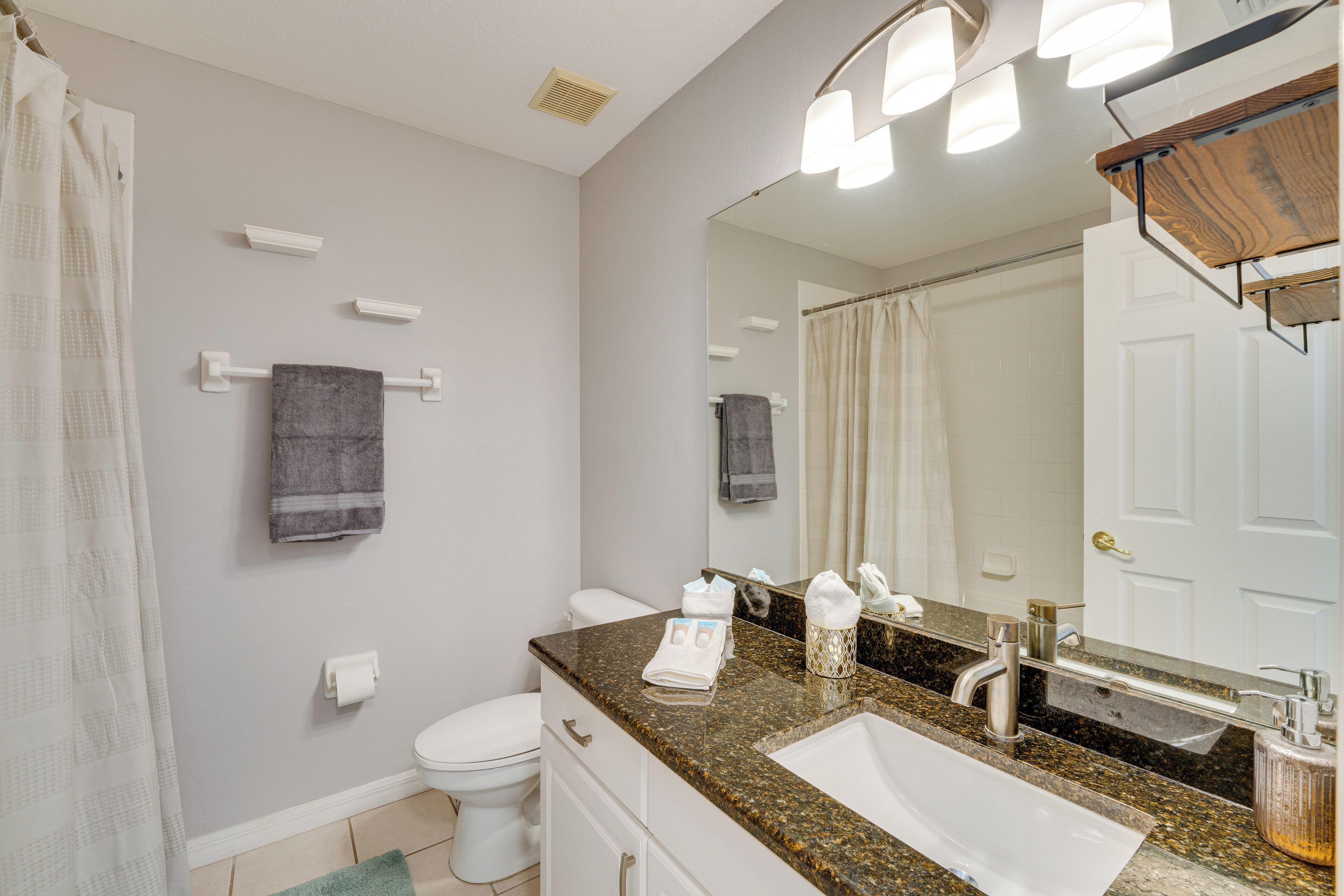 Une salle de bain moderne avec un comptoir en granit, un grand miroir, un lavabo blanc et des toilettes.