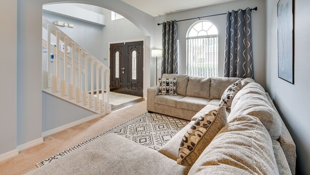 A living room with a sofa, a patterned rug, and a staircase leading to another room. - Disney-area Home w/ Private Pool in Davenport! (Davenport)