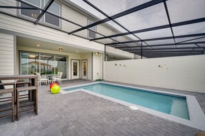 Une piscine dotée d’un patio couvert, de mobilier d’extérieur et offrant une vue sur un immeuble résidentiel.