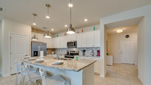 Une cuisine avec des armoires blanches, un comptoir en granit, des appareils en acier inoxydable et des luminaires suspendus.