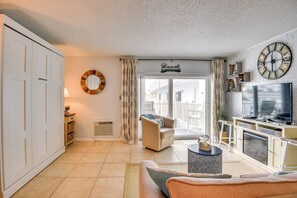 Een woonkamer met een bank, fauteuil, televisie en open haard.