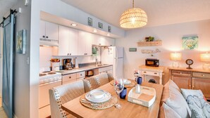 A modern kitchen with white cabinets, a dining table set with plates, and a hanging light fixture. - New Smyrna Beach Condo w/ Pool & Beach Access! (New Smyrna Beach)