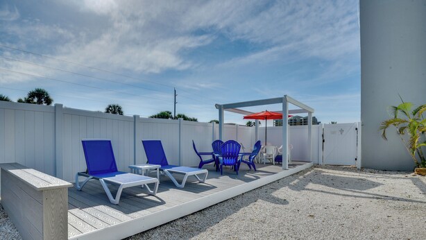 A covered outdoor seating area with blue chairs and a red umbrella. - New Smyrna Beach Condo w/ Pool & Beach Access! (New Smyrna Beach)